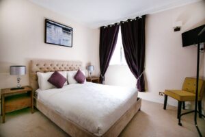 A double bedroom with white bedding, a dark upholstered headboard and floor-length curtains