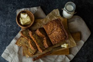Sliced bread on a wooden board with a pot of butter and a glass of milk