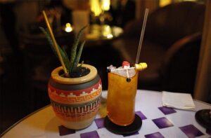 A garnished cocktail in a patterned mug on a bar table