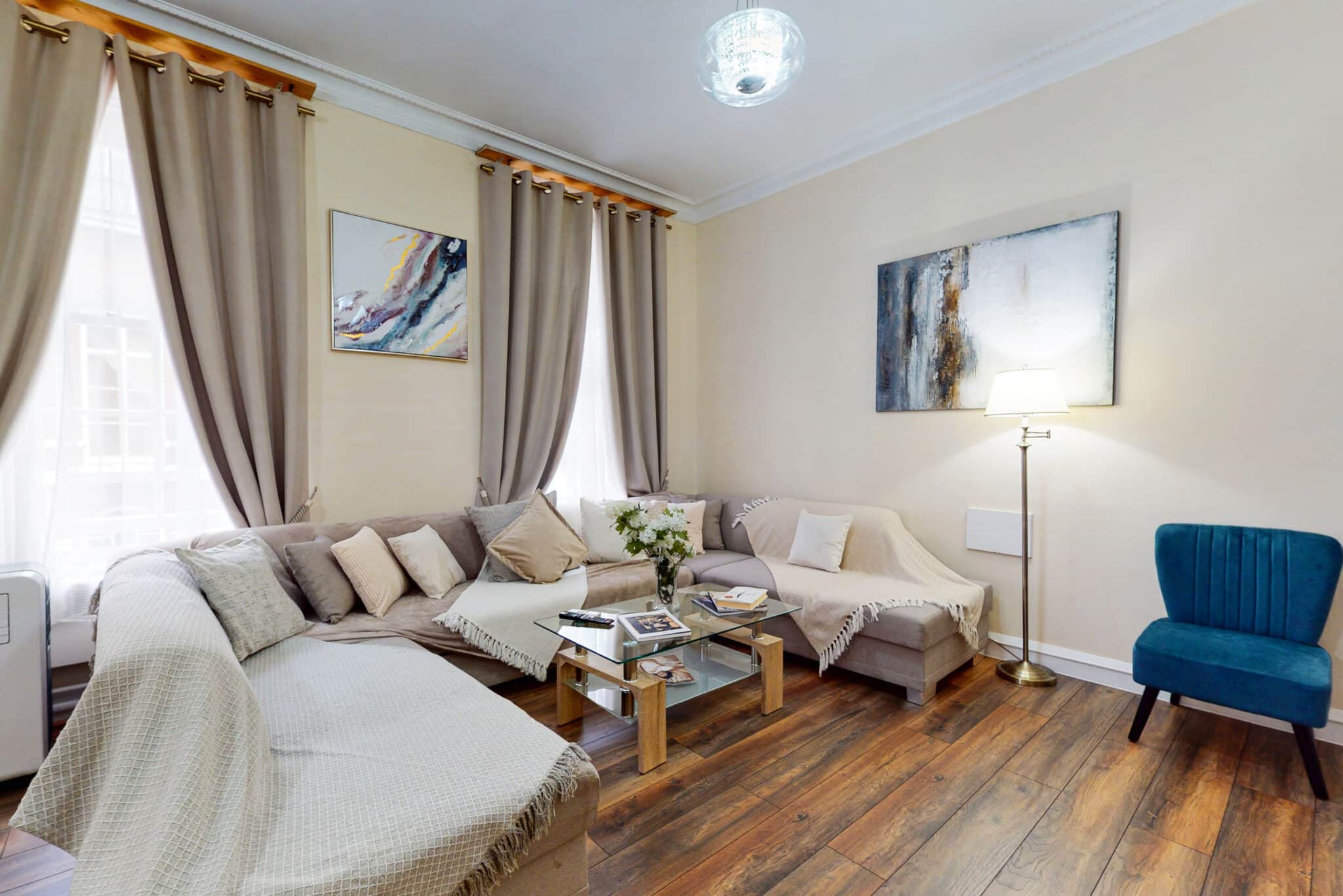 Living room with a cream corner sofa and full length curtains at Shaw House Mayfair