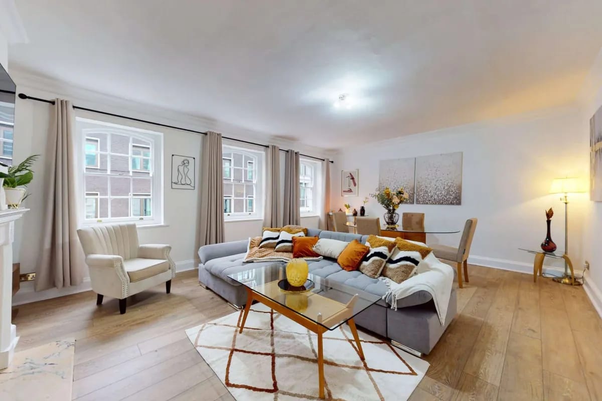 Living room with a grey corner sofa and two tall windows at 34-36 Clarges Street Mayfair