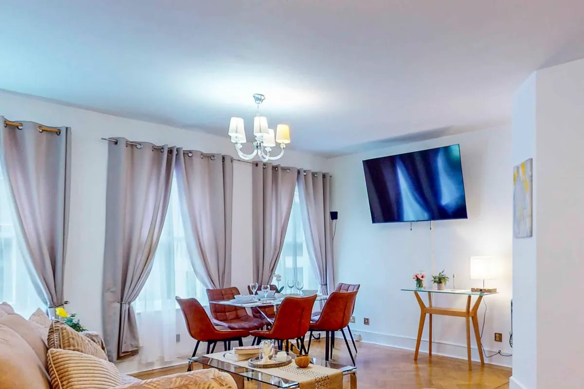 Sitting room with tall curtained windows and a wall mounted television at Mayfair Collection 37 Clarges Street